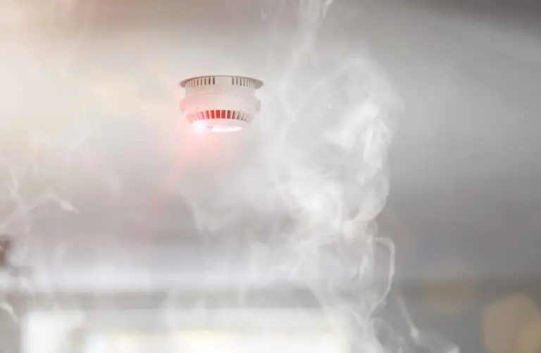 Smoke alarm activating with visible smoke in the room, signaling potential fire.